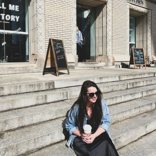 Woman drinking coffee while sitting on the steps of a bookstore