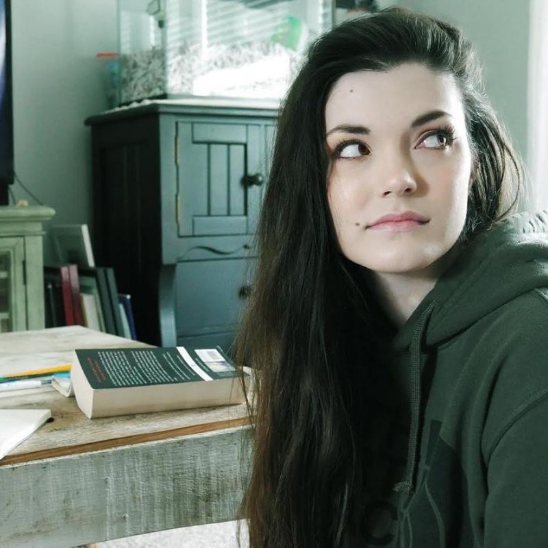 Woman in sweatshirt sitting in front of a table with a book and notebook on it.
