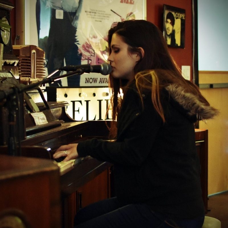 Woman sitting at a piano, playing and singing into a microphone.