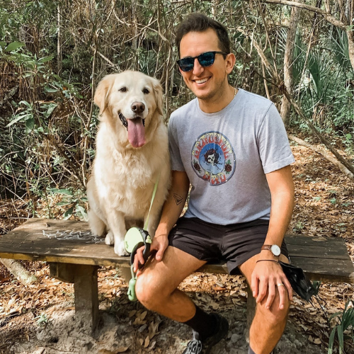 Steven Gallo sitting on a bench next to a golden retriever