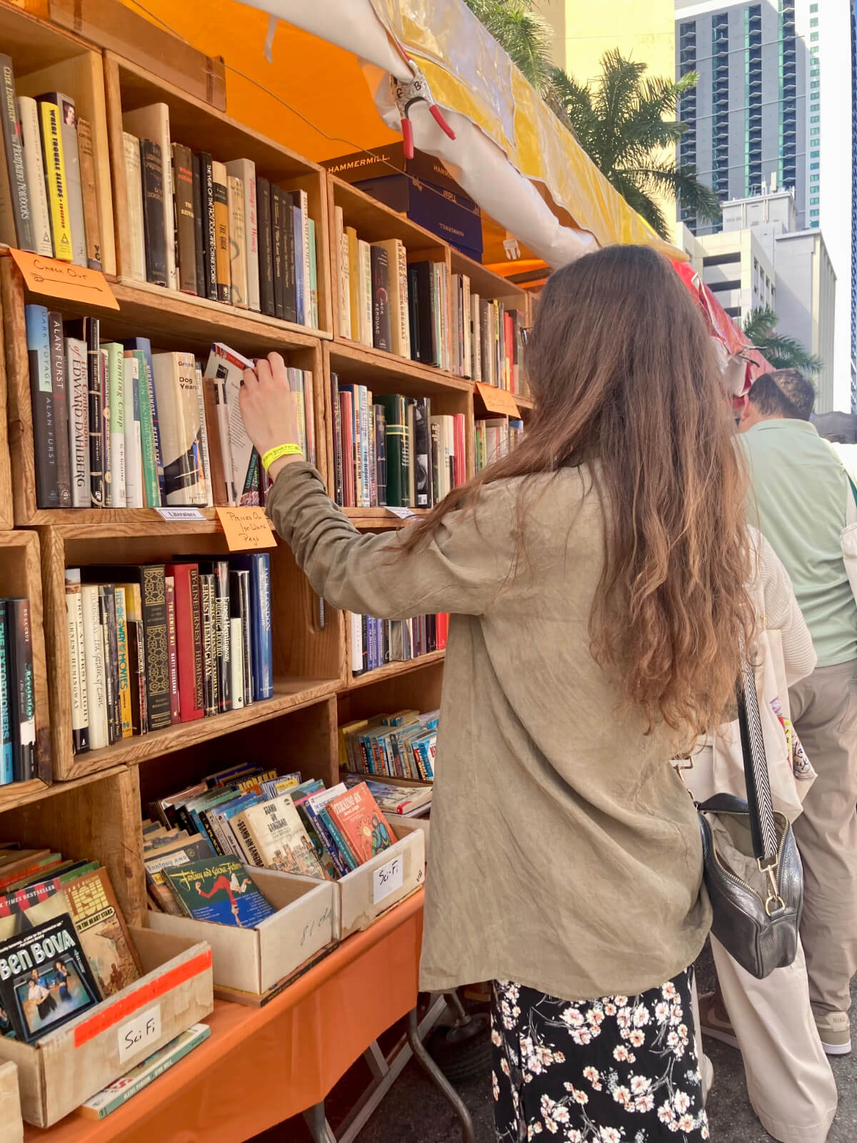 Raychel Lean at the Miami International Book Fair, browsing a shelf of books.