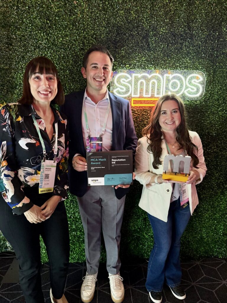 Reputation Ink team members with the 2026 SMPS “M” Award of Excellence trophy and MCA Merit Award for the S. Tipton Studio return-to-office brochure at the Amplify A|E|C conference
